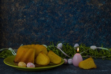 Easter bread on green plate and painted Easter eggs ion dark stone table decorated with green grass