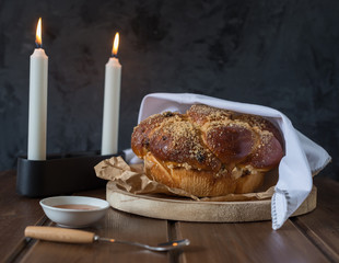 Sweet Challah bread on a wooded round plate on wooden brown table with honey and two candles on Shabbat evening making Kidush / black  background with copy space . close up