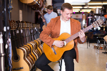 Young male seller showing guitar to boy client