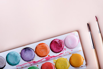 Watercolor in a palette with paint drops and a brush close-up on a pink background