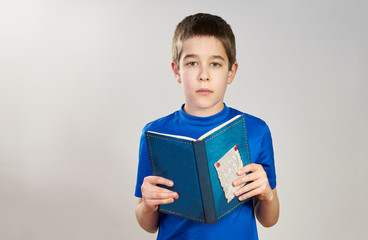 Portrait of a boy in a blue shirt holding a blue book and looking seriously