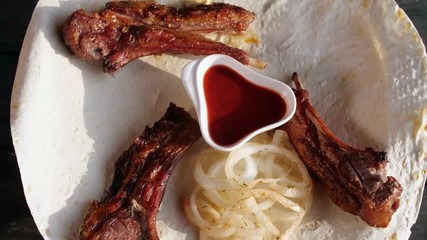 Lamb loin shish kebab with onions on pita close up. Rotates on a wooden background. Top view