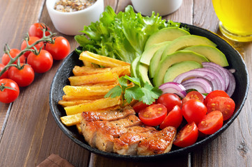 Roasted sliced pork steak, french fries and fresh vegetables on plate 