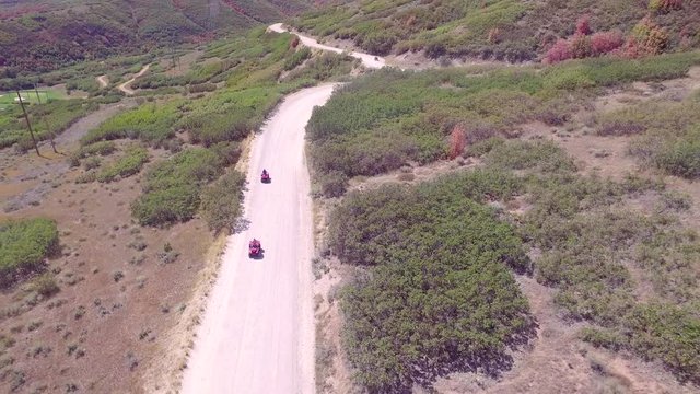 drone follows down a gravel road two atv four wheelers as they decend a mountain. In this aerial shot the drone follows two red atv 4-wheelers down a gravel mountain road during the autumn season.