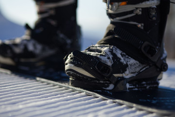 Snowboarder straps in his legs in snowboard boots in modern fast flow bindings with straps. - obrazy, fototapety, plakaty