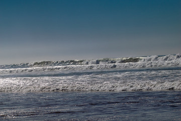 Clear blue skies and sunlight with Atlantic Ocean waves crashing onto sand beach with no people in Agadir, Morocco, Africa