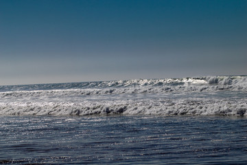 Clear blue skies and sunlight with Atlantic Ocean waves crashing onto sand beach with no people in Agadir, Morocco, Africa