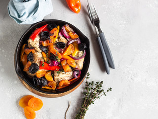 Grilled chicken with vegetables (bell pepper, carrot and onion) and dried fruits (apricots and prunes) in a cast-iron pan. Light gray background. Copy space. Healthy food.