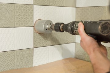 Preparatory work for the installation of an electrical outlet, man holding diamond tipped tile...