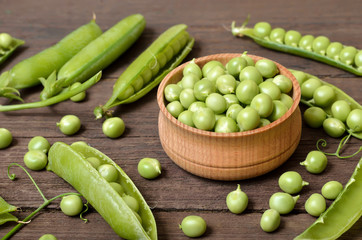 Green peas in wooden bowl, pods of green peas on wooden table