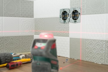 Electrician using infrared laser level to install electrical outlets. Renovation and construction...