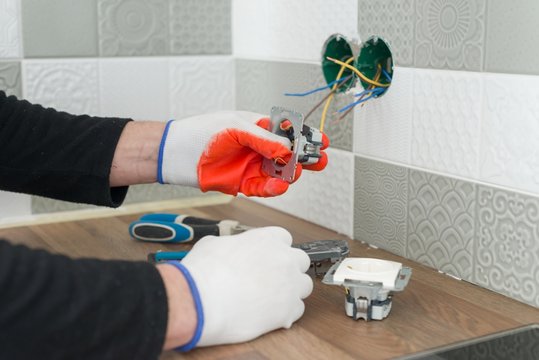 Renovation And Construction In Kitchen, Close-up Of Electricians Hand Installing Outlet On Wall With Ceramic Tiles Using Professional Tools