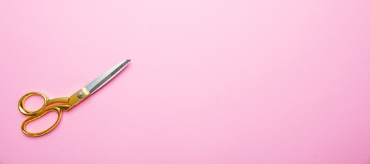 Scissors with golden handle on pink background, banne, copy space, top view