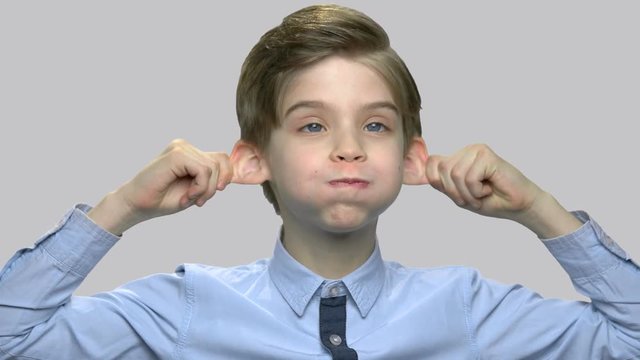 Caucasian boy making monkey face. Close up child boy grimacing against gray background.