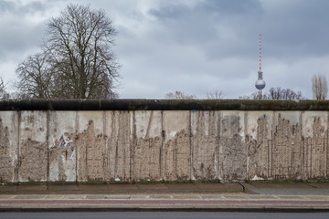 Front view of a section of the original Berlin Wall at the Berlin Wall Memorial (Berliner Mauer) in Berlin, Germany, on a cloudy day. Fernsehturm TV Tower is in the background.