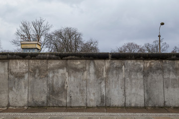 Front view of a section of the original Berlin Wall and watchtower at the Berlin Wall Memorial (Berliner Mauer) in Berlin, Germany, on a cloudy day. © tuomaslehtinen