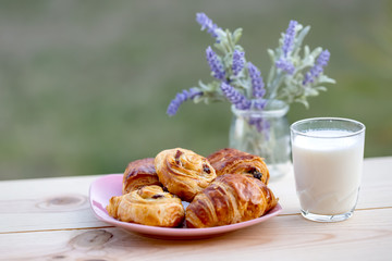 Buns with raisins and french croissant. A glass of milk on rustic table. Dinner in an orchard in summertime. Bouquet of lavender. Dessert. Soft focus. Summer twilight. Blurry background. Copy space.
