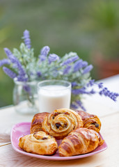 Buns with raisins and french croissant. A glass of milk on rustic table. Dinner in an orchard in summertime. Bouquet of lavender. Dessert. Soft focus. Summer twilight. Blurry background. Copy space.