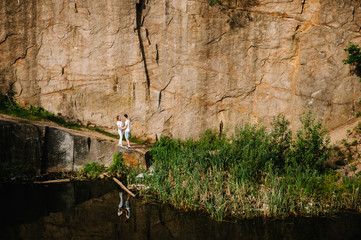 Reflection of people stand and hugs near the lake on the background of rocks. Landscape of an old flooded industrial granite quarry filled with water. Canyon. The nature of autumn.