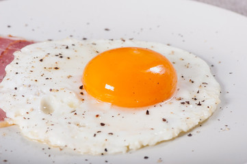 Fried egg and bacon on a light plate, breakfast food.