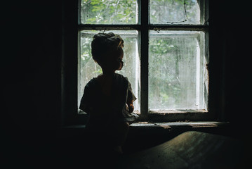 A terrible, bad plastic doll stands against the background of an old house and a window with cobwebs. Halloween and horror. Abandoned and lonely toy.