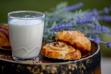 A glass of milk. Dessert. Buns with raisins on old wine barrel. Bouquet of lavender flowers. Dinner in an orchard. Summer twilight. Soft focus. Blurry background. Close-up. Macro.