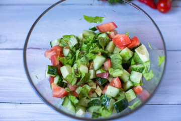 Salad of fresh tomato, cucumber and green salad with oil on a wooden background top view.