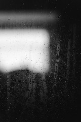 Closeup of condensation patterns on glass window, water droplets with light reflection and refraction, black and white abstract background