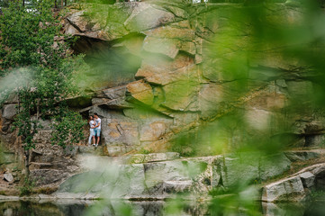 Fototapeta premium Young couple hugging a stone near the lake. A man and a woman stand against the background of the rocks. Top view. Nature. autumn. full length. looking at each other.