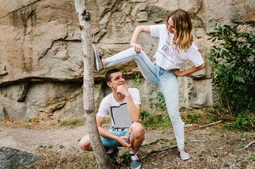Strongman girl standing and poses. The man is sitting between legs of girl. The woman put her foot on the tree. Portrait of a joke people against the background of the mountain on nature. Close up.