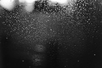 Closeup of condensation patterns on glass window, water droplets with light reflection and refraction, black and white abstract background