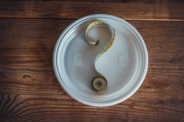 Tape measure forming the shape of question mark in a plate on wooden table