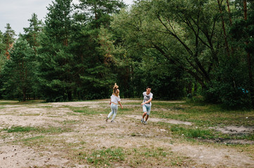 Young couple running away and having fun on the background on the nature. A woman catches her husband against the background of trees and fir trees.