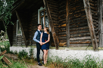 A man hugs back a tender woman. full length. looking at each other. on the background nature. Young lovers couple standing near an old wooden stylish house.