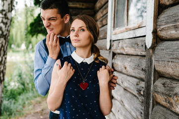 Man hug a woman in back against the backdrop of a wooden wall of the house. close up. Heart necklace around his neck near breast. love. half length. facial expression, frowns and make a grimace.