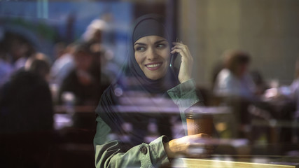 Attractive young Arab female talking on phone, spending free time in cafe, relax