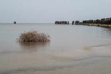 calm sea beach in summer with large rocks and wooden poles from old breakewater in the sea