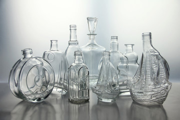 Empty glass bottles. Transparent forms for cold drinks, randomly presented and isolated on a gray background.