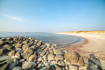 calm sea beach in summer with large rocks and wooden poles from old breakewater in the sea
