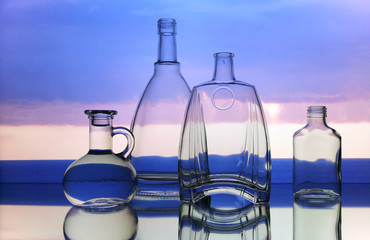 Empty glass bottles. Transparent forms for cold drinks, randomly presented and on a sky background. Presentation of glass forms in the industrial production of glass.