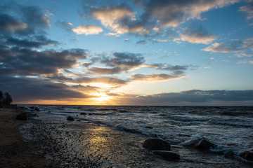 dramatic sunset over sea beach with rocks and stormy water