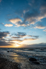 Fototapeta premium dramatic sunset over sea beach with rocks and stormy water