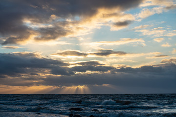 dramatic sunset over sea beach with rocks and stormy water