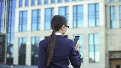 Female office worker reading message on smartphone outdoors, social network app