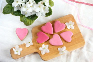Obraz na płótnie Canvas Pretty girlish flat style with gently pink hearts biscuits cookies with white violets blooming flowers and satin ribbon top view.14 february valentine's day gift treat