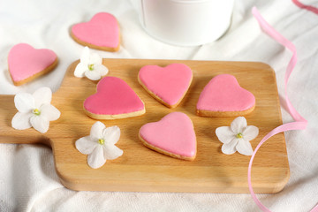 Fototapeta na wymiar Pretty girlish flat style with group of gently pink hearts biscuits cookies with white violets blooming flowers and satin ribbon top view.14 february valentine's day and wedding bonboniers gift treat