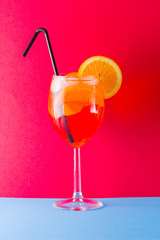 Cocktail aperol spritz on red blue background. Summer alcoholic cocktail with orange slices. Aperol spritz on colored background. Coral colored cocktail in minimalism style