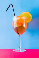 Cocktail aperol spritz on red blue background. Summer alcoholic cocktail with orange slices. Aperol spritz on colored background. Coral colored cocktail in minimalism style