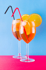 Cocktail aperol spritz on red blue background. Summer alcoholic cocktail with orange slices. Aperol spritz on colored background. Coral colored cocktail in minimalism style