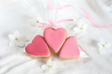 Pretty  girlish flat style with group of gently pink hearts biscuits cookies with white violets blooming flowers and satin ribbon top view.14 february valentine's day and wedding bonboniers gift treat